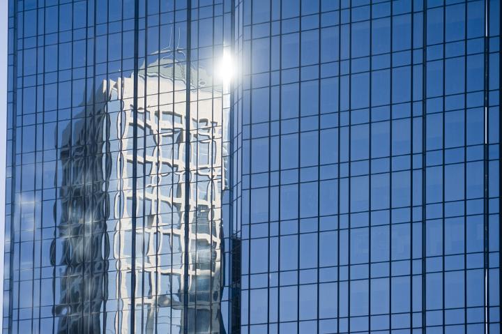 Urban office building reflected in the facade made of glass of a skyscraper, in a sunny day