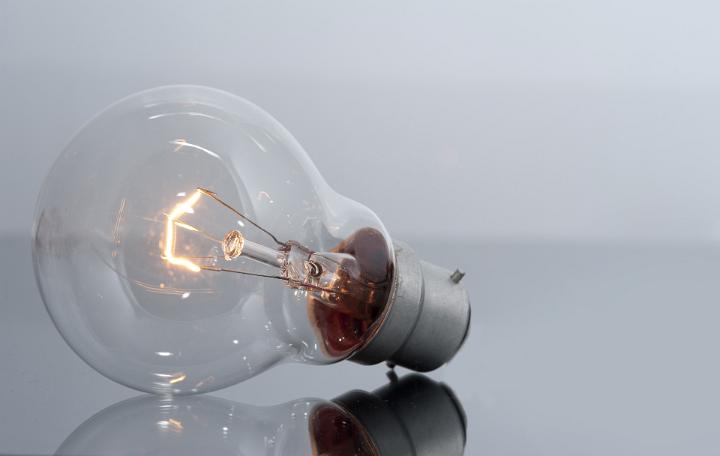 Close Up of Clear Light Bulb with Glowing Filament on Grey Background in Idea Concept Image