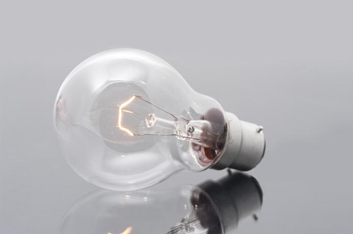 Domestic light bulb with a bayonet fitting and a glowing filament on a reflective grey surface for power and energy or bright ideas concepts