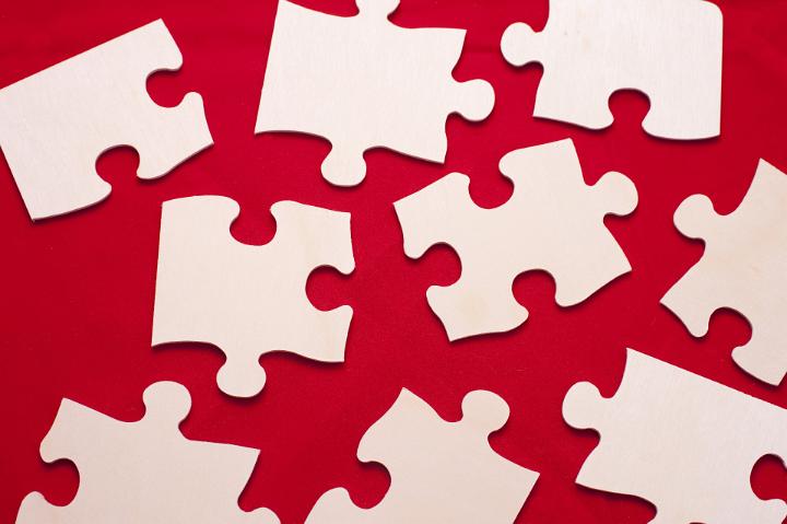 Overhead view of a group of differently shaped scattered white puzzle pieces on a red background in a problem solving concept
