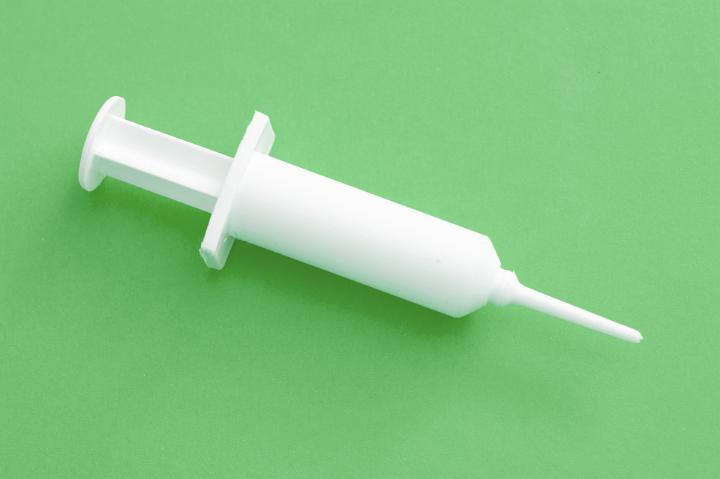 Small platic syringe on green background concept of innocculation, pest and disease control