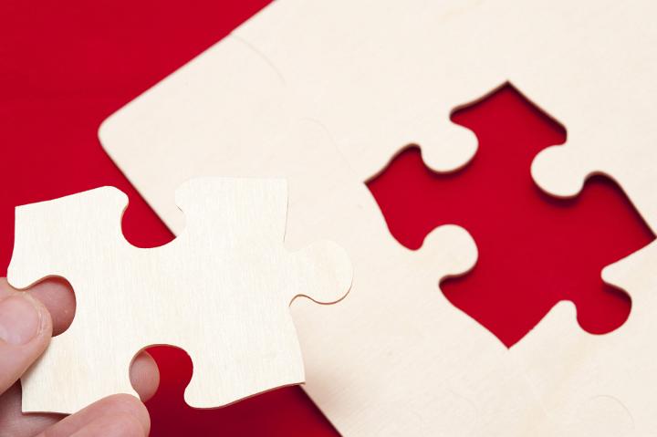 Conceptual Man Holding White Puzzle Piece to Complete the Puzzle on the Red Table