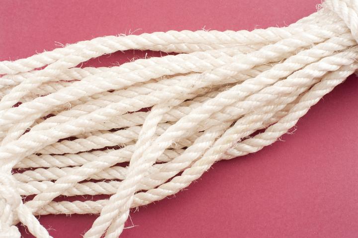 New clean white braided rope in a neat coil lying on a red background with copyspace