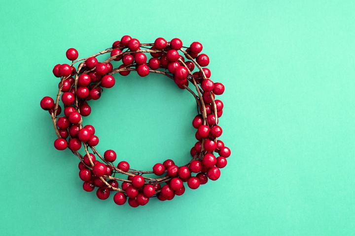 A decorative red berry Christmas wreath on a plain green background with copy space.