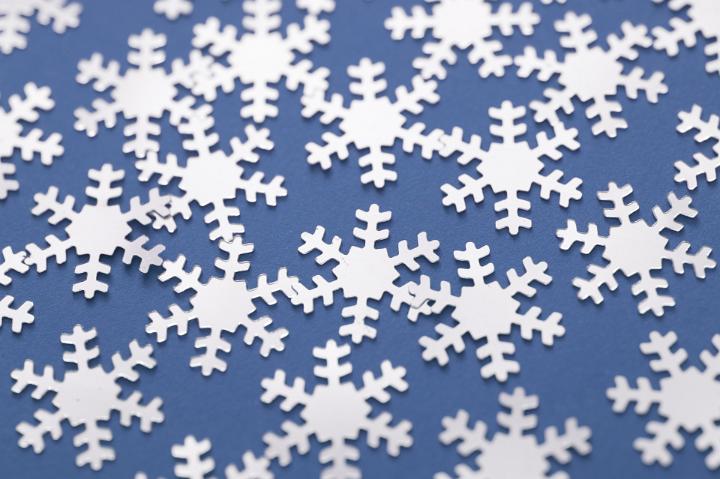 Christmas background of scattered white snowflakes on a cool blue wintry background, full frame