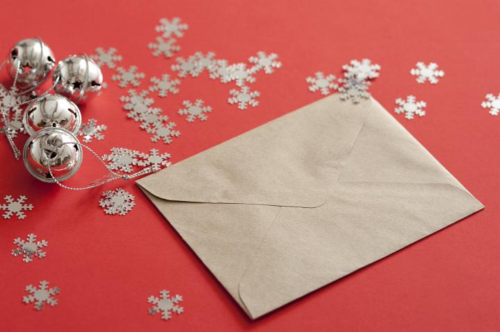 Close up Christmas Card in a Brown Envelope on Top of Orange Table with Snow Flakes and Bells