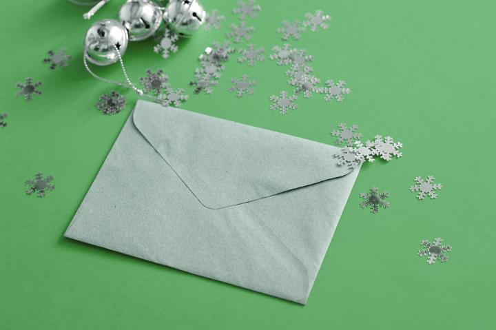 Green sealed Christmas letter and decorations with scattered snowflakes and silver bells on a green background for festive correspondence