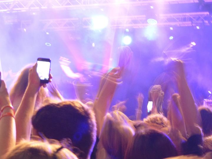 Music audience at a live concert cheering and taking photos on their mobile phones , backlit by the bright spot lights viewed from behind