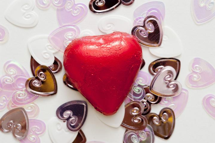 One red, chocolate valentine heart sits on top of a pile of smaller wedding heart decorations.