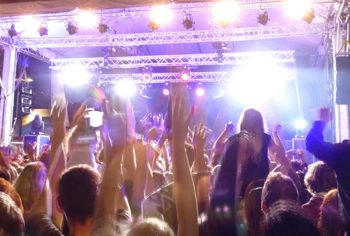 People with raised hands attending a live performance on the stage during an entertaining concert, rear view