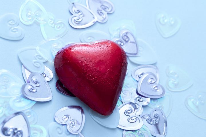 A single, red valentine chocolate on metallic wedding heart confetti decorations.