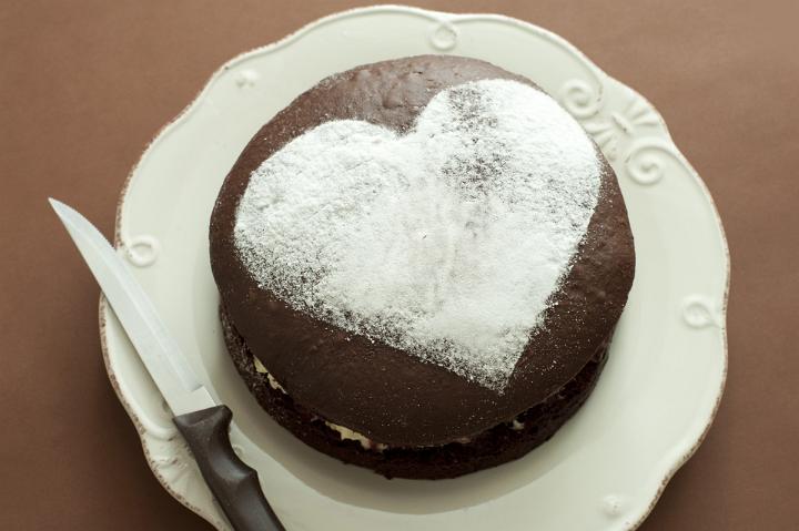 Close up Valentine Brown Cake on Plate with Heart Shape on Top. Isolated on Brown Background.