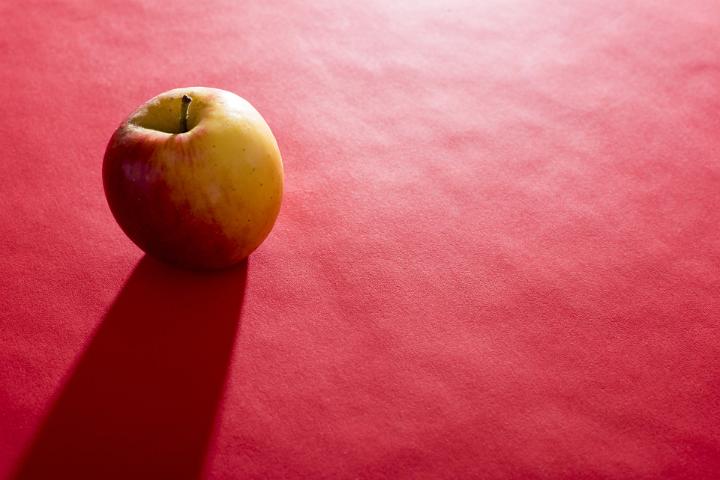A fresh apple back lit in bright light on a plain red background with copy space.