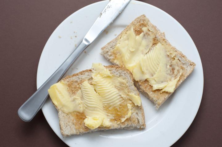 Two slices of fresh buttered white toast with a bread knife served on a plate for morning breakfast, overhead view