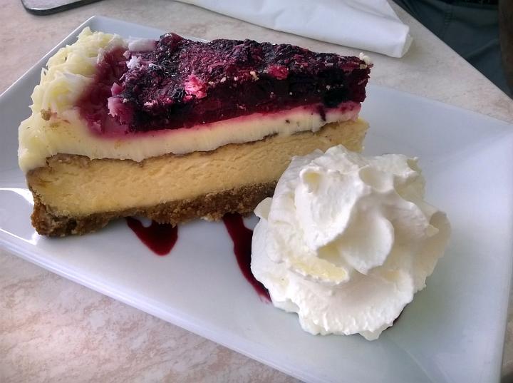 A rich berry cheesecake slice with fluffy whipped cream served on a white plate.