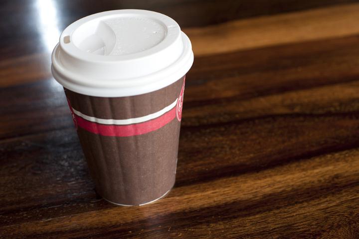 Closed brown disposable takeaway coffee cup from a restaurant or cafeteria on a wooden table with copyspace