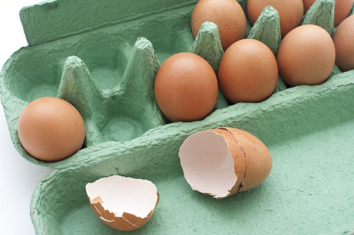 Open green box of healthy brown farm eggs with an empty eggshell broken open lying in the front in a cooking and baking concept
