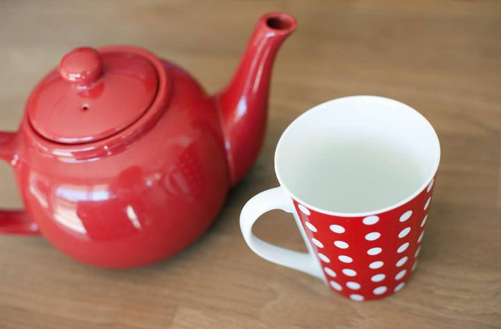 High angle view of a colorful red polka dot ceramic mug and teapot on a brown background