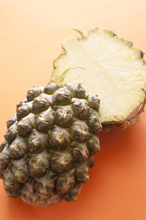 A fresh pineapple cut in half and isolated on a bright orange background with copy space.