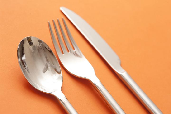 Close Up of Set of Silver Cutlery Dinner Service Including Spoon, Fork, and Knife on Orange Background