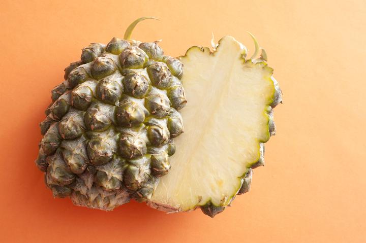 A fresh pineapple, sliced in half, isolated on a bright orange background.