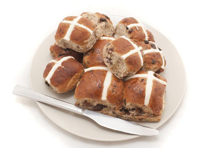 Still Life of Baked Hot Cross Buns Piled on White Plate with Silver Knife for Breakfast on White Background
