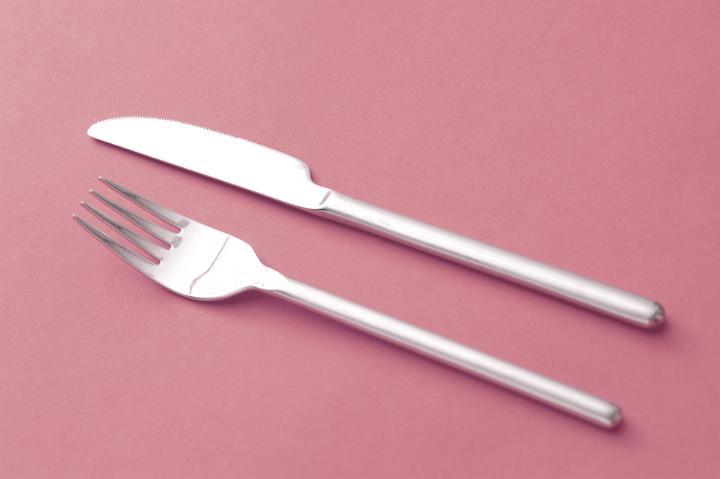 Simple design silver knife and fork lying side by side on a red background diagonally across the frame
