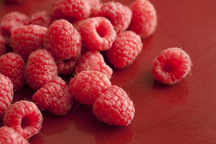 Delicious ripe raspberries close-up on red surface, captured in selective focus from high angle