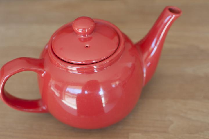 Red ceramic teapot with a bulbous form and shiny glaze on a wooden table, high angle view