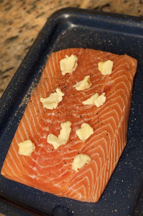 Fresh raw salmon fillet ready for baking or grilling in the oven daubed with blobs of butter and seasoning