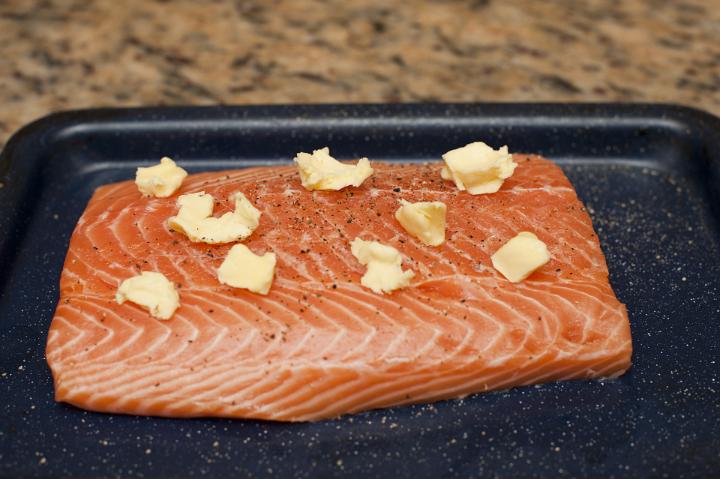 Raw Filet of Salmon Seasoned with Pepper and Pats of Butter on Baking Pan on Counter Top
