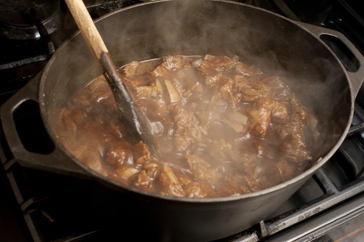 Cooking a pot of wholesome beef stew in gravy in a saucepan over a gas hob stirring it with a wooden spoon
