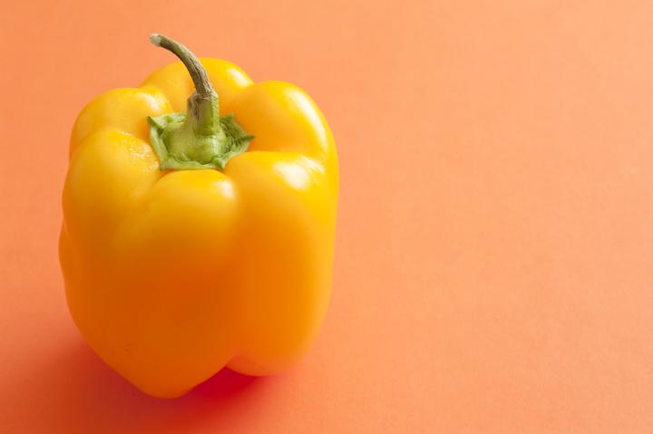 Yellow pepper on orange surface background with copy space, close-up from high angle
