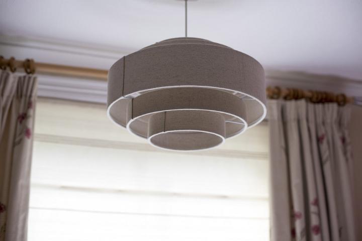 A white, contemporary ceiling light shade hanging from the interior of a modern home with hanging curtains.