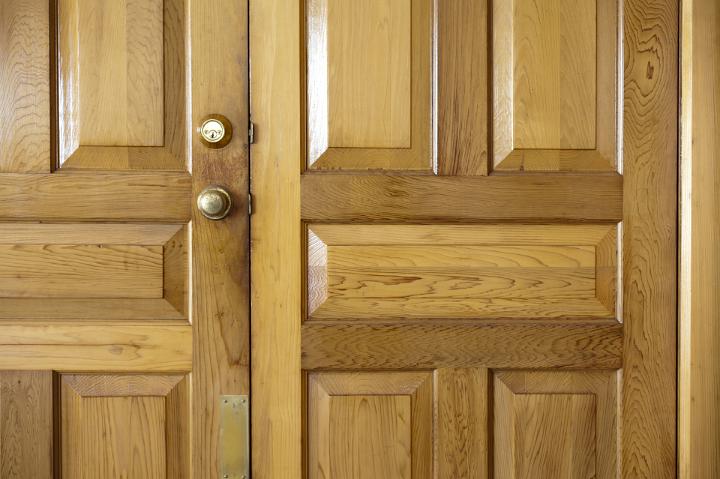 Close up of the panels on a set of natural wood double front doors to a home with a brass handle and lock