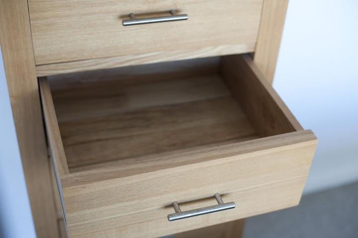 High angle view of an empty open wooden drawer in a small natural wood cabinet against a white indoor wall