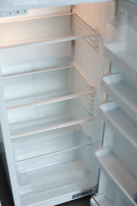 Interior of an empty white fridge with the door standing open to reveal the shelves and fittings, close up view