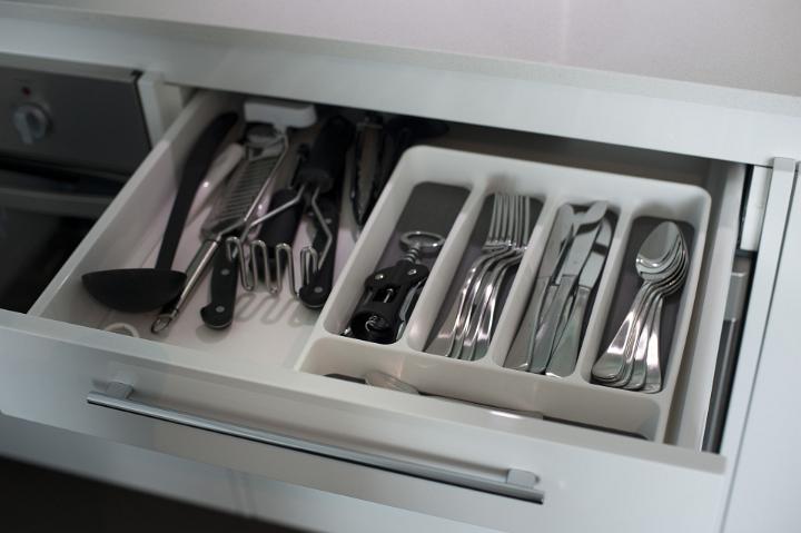 Open kitchen drawer with fitted compartments filled with cutlery and utensils in a white cabinet