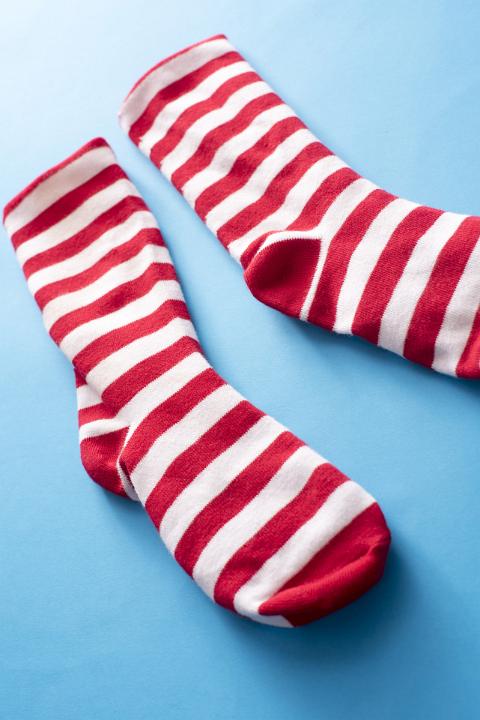 A pair of red and white striped Christmas Santa socks isolated on a plain blue background.