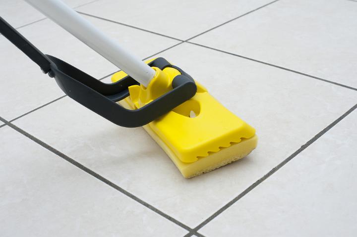 Mopping the white tiled kitchen or bathroom floor using a colorful yellow plastic squeegee in a household chores, cleanliness and hygiene concept