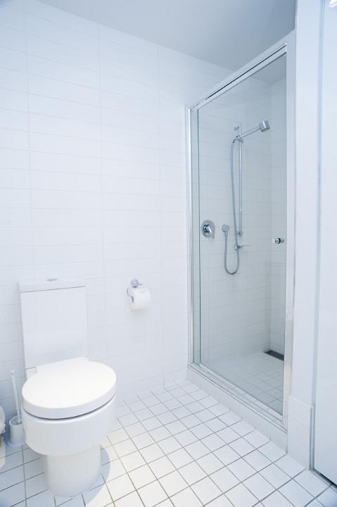 Interior of a clean fresh white bathroom with a tiled floor, shower, cabinets and toilet