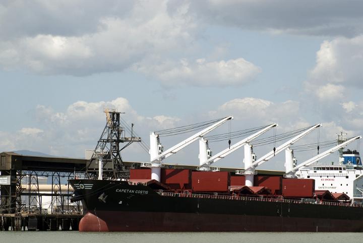 Large industrial cranes on the wharf at a shipping terminal for loading cargo on a bulk carrier, freighter or tanker with a ship docked at the quay