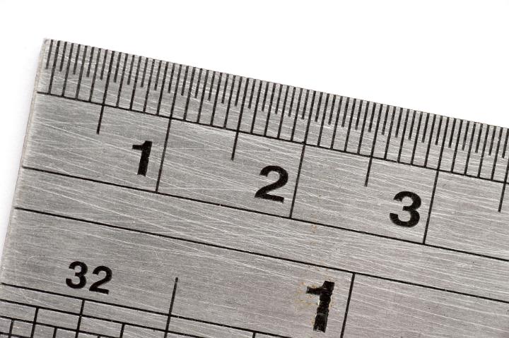 Close up of the end of a steel ruler marked with both inches and centimetres isolated on white