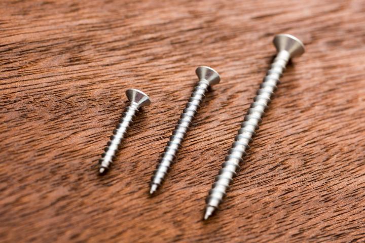 Three screws in different sizes lying on wooden background