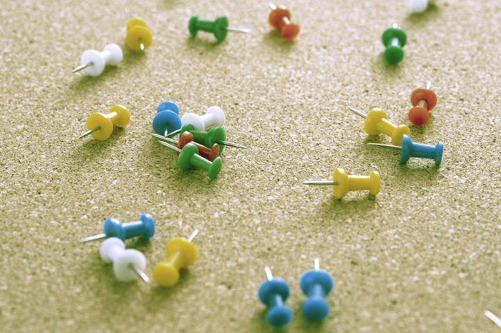 Close up Scattered Colored Map Pins on Top of Brown Cork Board