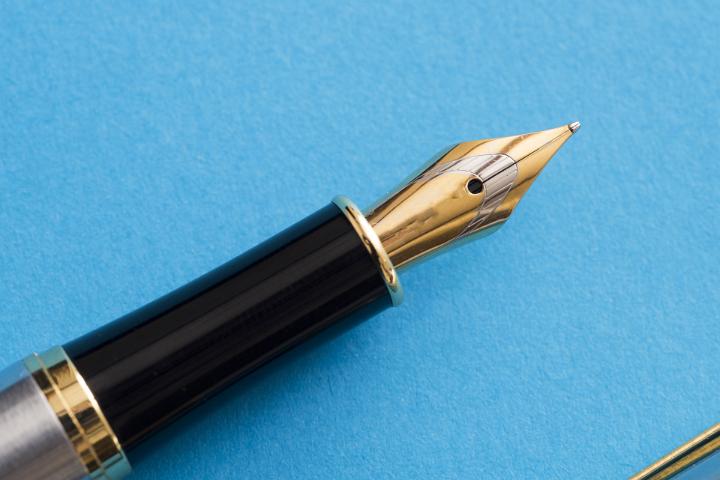 Close up of a calligraphy fountain pen tip isolated on a blue background with copy space.