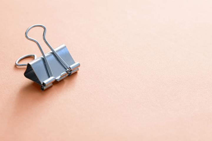 A single, metal office paper bull clip isolated on a plain background with copy space.