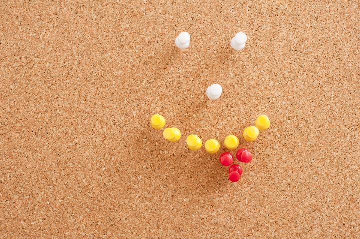Close up Conceptual White, Yellow and Red Pins on Brown Cork Board Forming Smiley with Tongue Out.