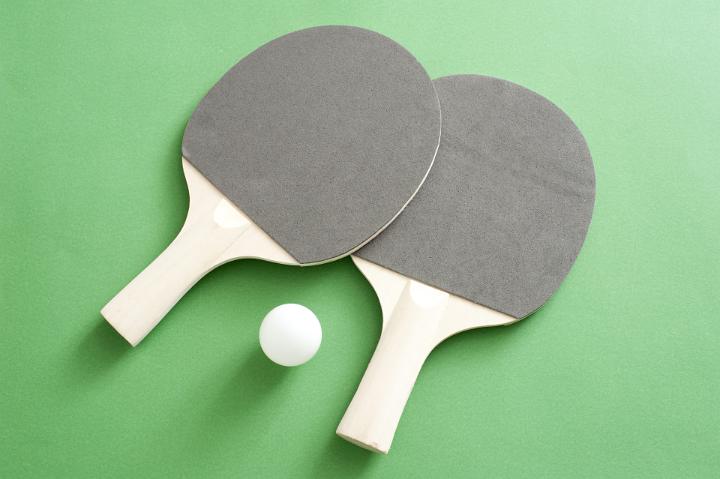 Two table tennis bats with a ball lying ready on a green wooden table for a game of indoor table tennis