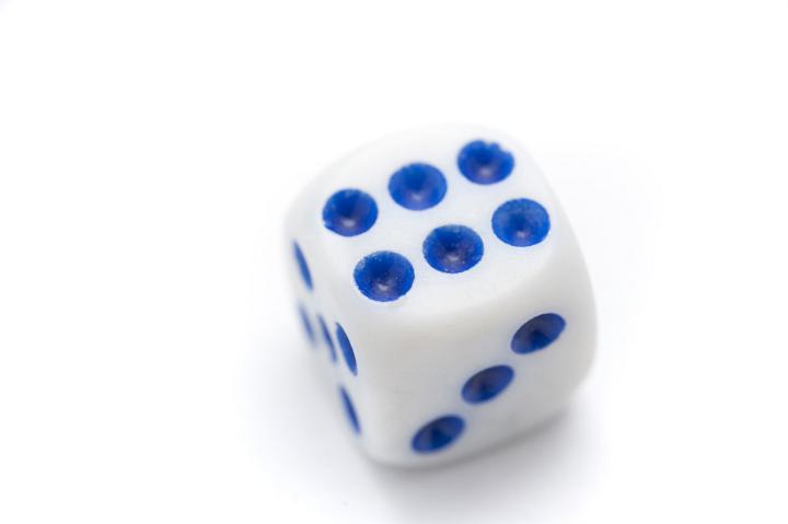 Single dice showing a blue number six lying on a white background in a gambling and casino concept